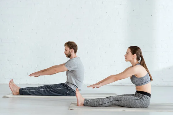 Vista lateral del hombre y la mujer practicando yoga en pose de flexión sentada hacia adelante - foto de stock