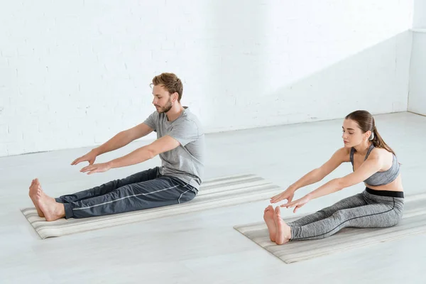 Joven hombre y mujer practicando yoga en pose de flexión sentada hacia adelante - foto de stock