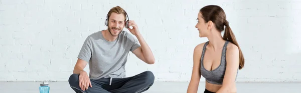 Панорамний знімок молодої жінки, яка дивиться на веселого чоловіка в навушниках — стокове фото