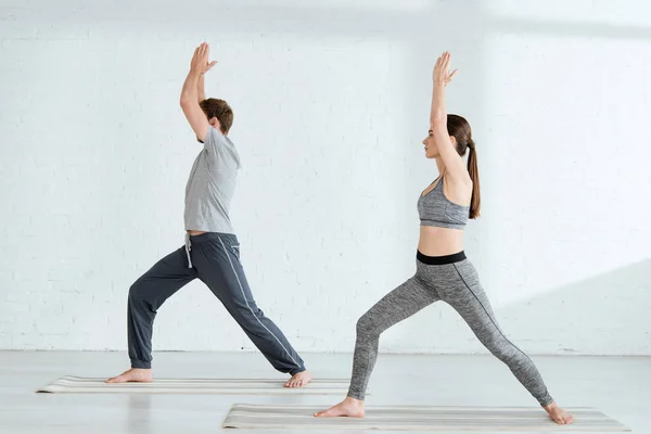 Side view of young man and woman practicing yoga in warrior I pose — Stock Photo