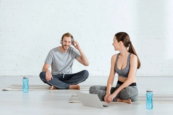 Hombre alegre en auriculares y mujer con portátil sentado en poses fáciles - foto de stock