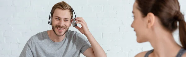 Selective focus of young woman looking at cheerful man in headphones, panoramic shot — Stock Photo