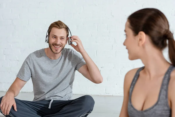 Enfoque selectivo de la mujer joven mirando hombre alegre en auriculares sentados en pose fácil - foto de stock