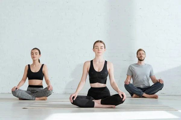 Hombres y mujeres jóvenes practicando yoga en pose de medio loto - foto de stock