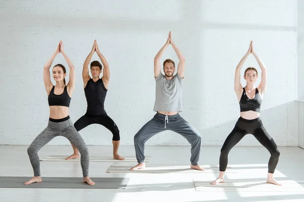Young people in sportswear practicing yoga in goddess pose with raised prayer hands — Stock Photo