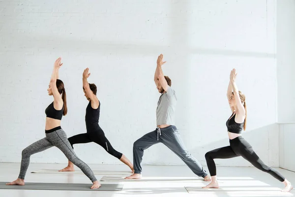 Vista laterale dei giovani in abbigliamento sportivo praticare yoga in guerriero posa — Foto stock