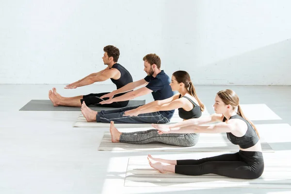 Jóvenes en ropa deportiva practicando yoga en pose de flexión sentada hacia adelante - foto de stock