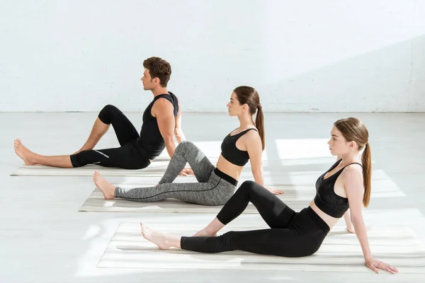 Mujeres jóvenes y hombres que practican yoga en el personal posan con la rodilla doblada - foto de stock