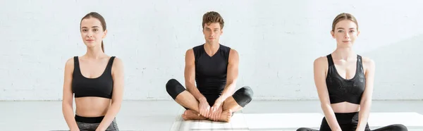 Colpo panoramico di giovani donne e uomo che praticano yoga in posa mezzo loto — Foto stock