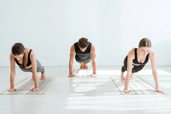 Mujeres jóvenes y hombres practicando yoga en pose de tablón - foto de stock