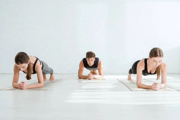 Mujeres jóvenes y hombres practicando yoga en la pose de la tabla del antebrazo - foto de stock