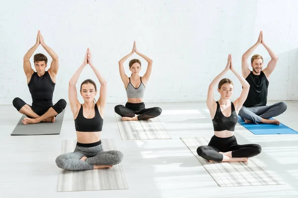 Five young people meditating in half lotus pose with raised prayer hands — Stock Photo