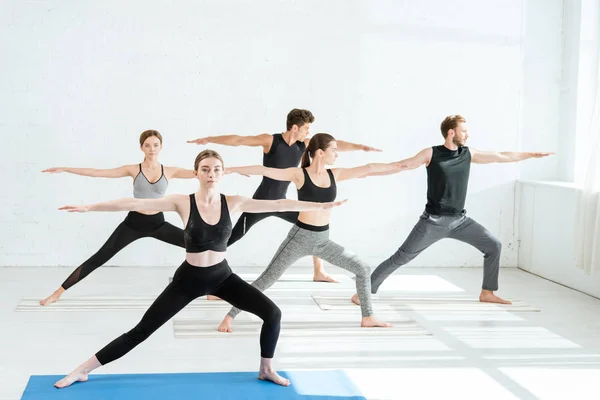 Пять юношей и девушек, практикующих йогу в позе воина II — стоковое фото