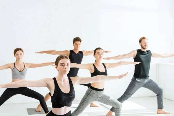 Cinq jeunes pratiquant le yoga en posture guerrière II — Photo de stock