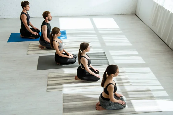 Vista de ángulo alto de cinco jóvenes meditando en pose de rayo - foto de stock