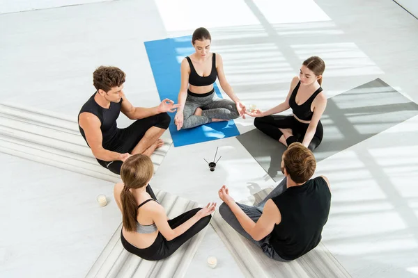 Cinco jóvenes sentados en círculo y meditando en actitud fácil cerca de velas y palos aromáticos - foto de stock