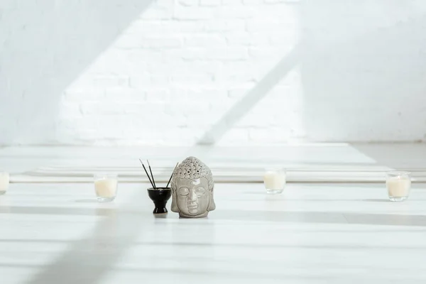 Cabeça decorativa buddha perto de paus aromáticos e velas no chão branco — Fotografia de Stock