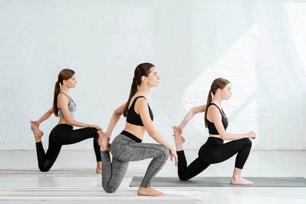 Vista lateral de tres mujeres jóvenes practicando yoga en pose de sirena - foto de stock