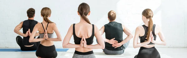 Vista posterior de hombres y mujeres jóvenes meditando en pose de rayo con las manos oradas detrás de la espalda, tiro panorámico - foto de stock