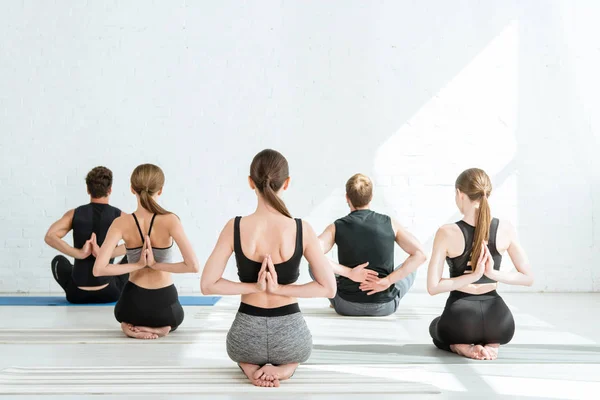 Back view of young men and women meditating in thunderbolt pose with prayed hands behind back — Stock Photo