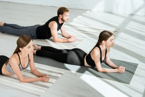 Dos mujeres jóvenes y un hombre practicando yoga en pose de esfinge - foto de stock