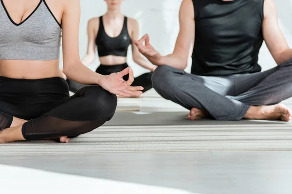 Partial view of young women and man practicing yoga in half lotus pose — Stock Photo