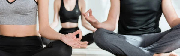 Vista ritagliata di giovani donne e uomo che praticano yoga in posa a metà loto, scatto panoramico — Foto stock