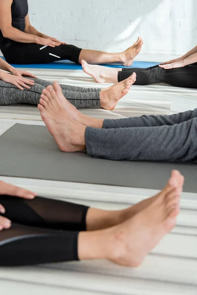 Vista recortada de personas descalzas sentadas en colchonetas de yoga en pose de personal - foto de stock