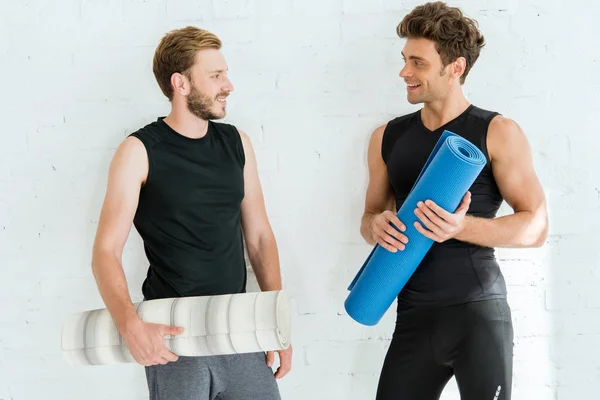 Двоє молодих усміхнених чоловіків розмовляють, тримаючи йога килимки — стокове фото