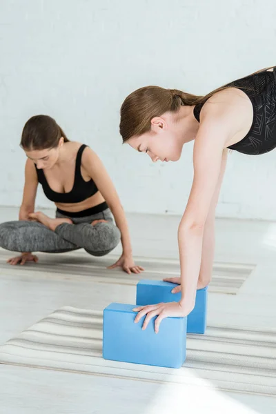 Mujer joven practicando yoga mientras se apoya en gradas con las manos cerca de la chica en posición de patanes elevados - foto de stock