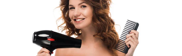 Tiro panorâmico de menina encaracolado feliz segurando secador de cabelo e escova de cabelo isolado no branco — Fotografia de Stock