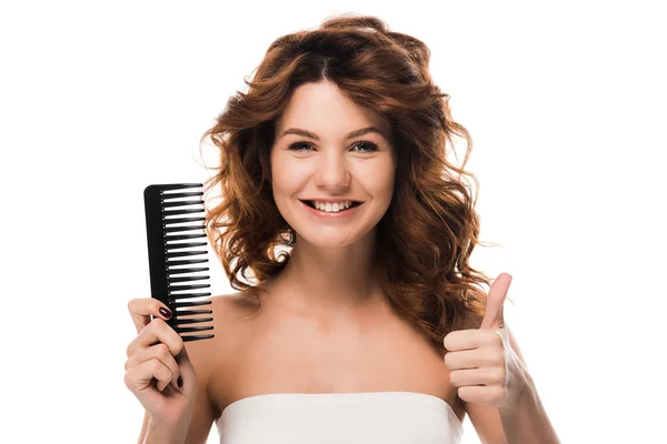Felice ragazza con i capelli ricci tenendo pennello per capelli e mostrando pollice in alto isolato su bianco — Foto stock