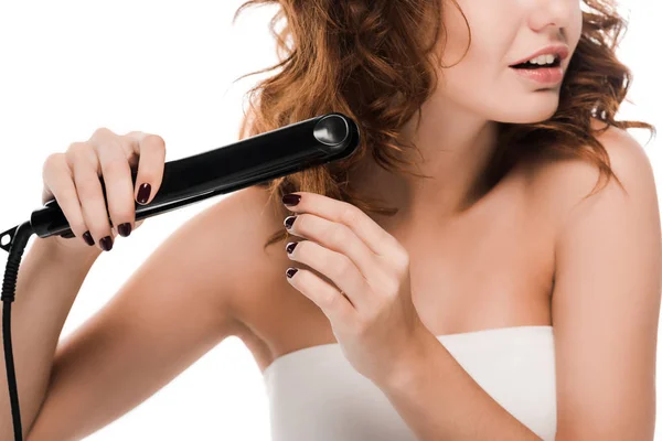 Vista ritagliata di sorpreso donna riccia utilizzando raddrizzatore di capelli isolato su bianco — Foto stock