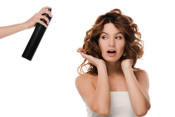 Vista cortada de mulher segurando frasco de spray de cabelo perto atraente menina encaracolado isolado no branco — Fotografia de Stock