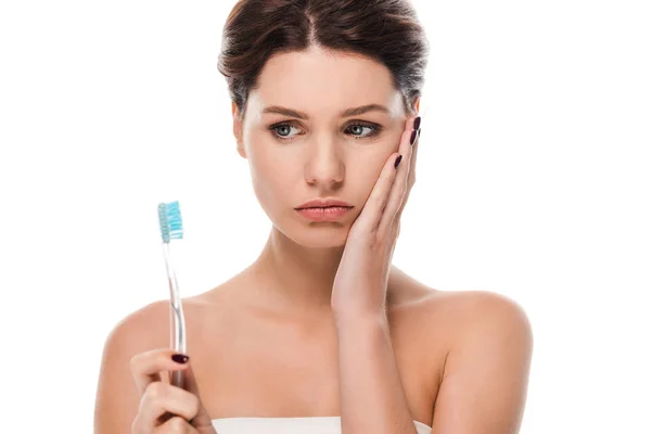 Сумна молода жінка торкається обличчя, тримаючи зубну щітку ізольовано на білому — стокове фото