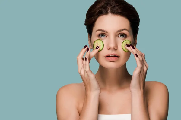 Séduisante femme touchant concombres sur le visage isolé sur bleu — Photo de stock