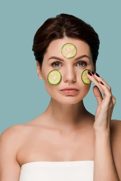 Young attractive woman touching cucumber on face isolated on blue — Stock Photo