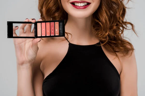 Cropped view of happy woman holding set of lip gloss isolated on grey — Stock Photo