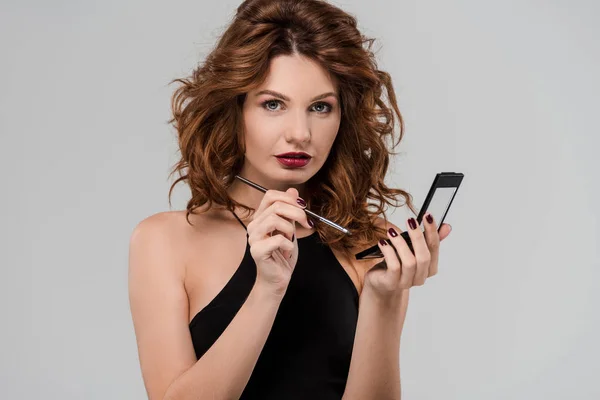 Attractive curly woman holding cosmetic brush isolated on grey — Stock Photo