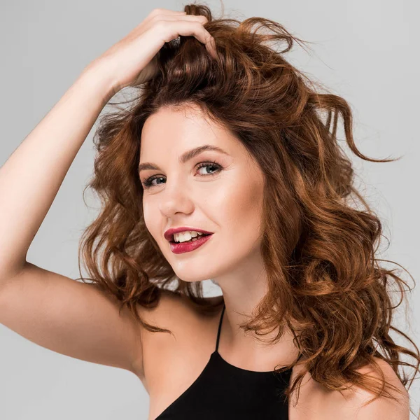 Fröhliche Frau berührt lockiges Haar isoliert auf grau — Stockfoto