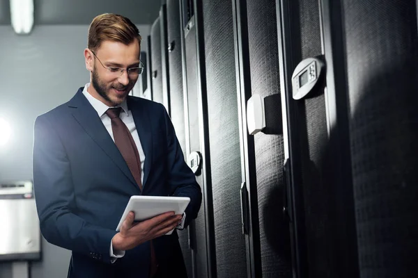 Selective focus of cheerful businessman in suit using digital tablet in data center — Stock Photo