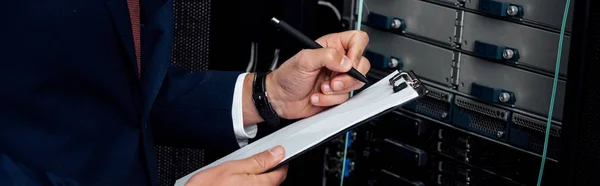 Panoramic shot of man in suit holding clipboard and pen in data center — Stock Photo