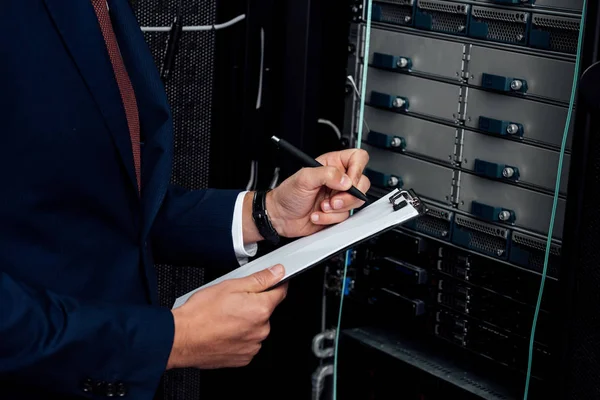 Cropped view of man in suit holding clipboard and pen in data center — Stock Photo