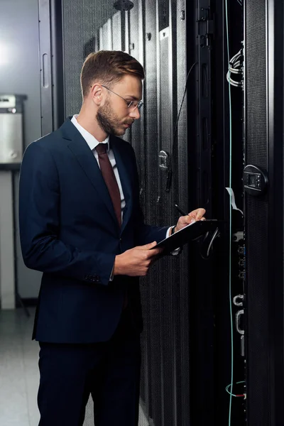 Handsome businessman in suit holding clipboard and pen in data center — Stock Photo