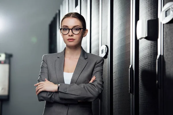 Enfoque selectivo de atractiva mujer de negocios en gafas de pie con brazos cruzados en el centro de datos - foto de stock