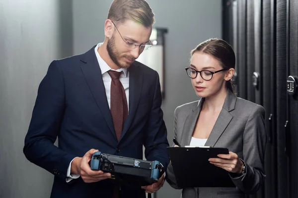 Homem de negócios bonito segurando reflectometer perto de empresária em data center — Fotografia de Stock