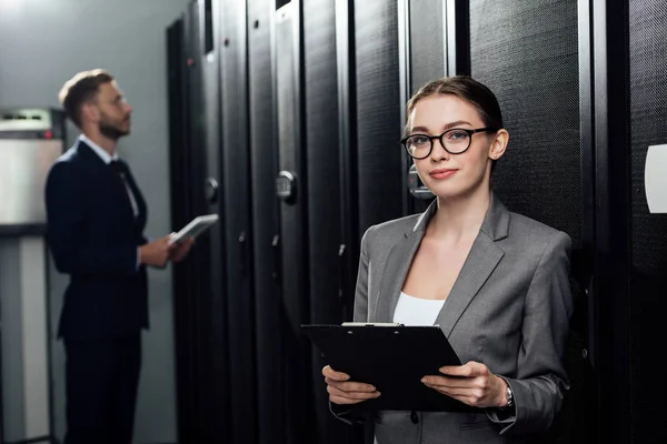 Selektiver Fokus der attraktiven Geschäftsfrau mit Brille, die im Datengalopp in die Kamera schaut, neben dem bärtigen Geschäftsmann — Stockfoto