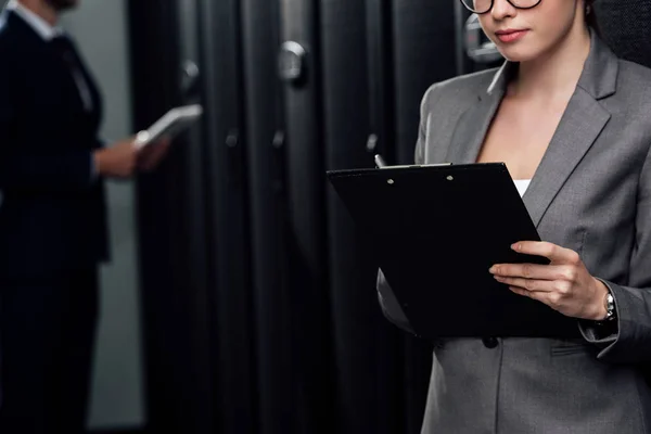 Abgeschnittene Ansicht von Geschäftsfrau mit Klemmbrett in der Nähe von Geschäftsmann und Server-Racks — Stockfoto