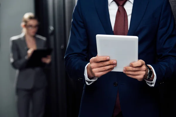 Visão cortada de empresário segurando tablet digital perto de empresária e racks de servidor — Fotografia de Stock