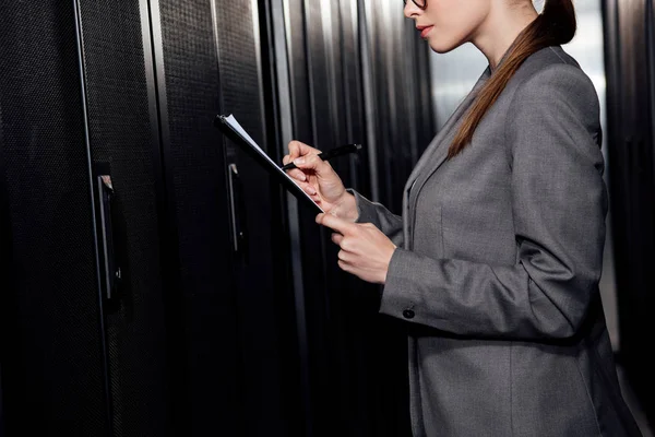 Cropped view of businesswoman holding pen near clipboard in data center — Stock Photo